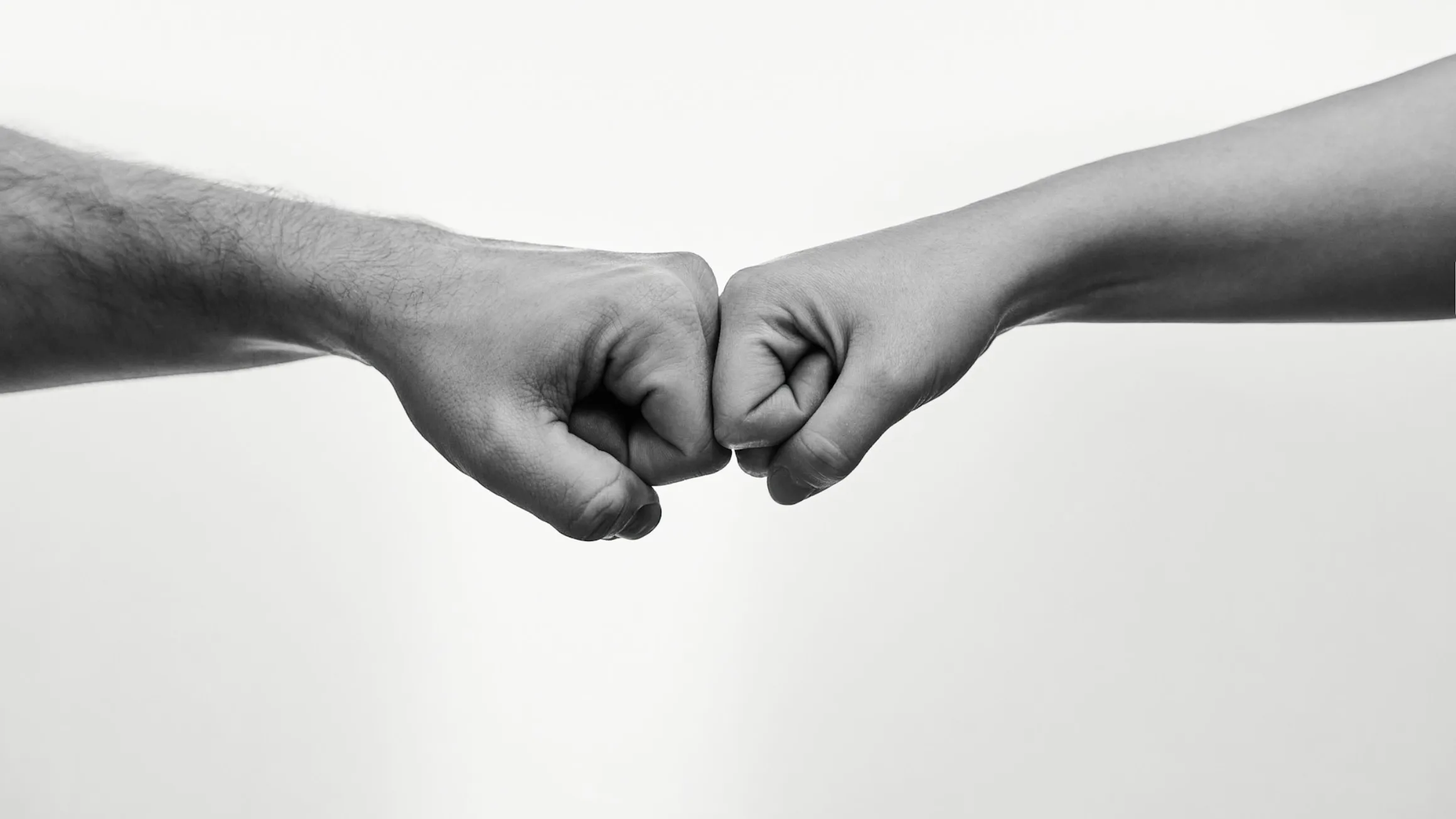 Zwei Hände stoßen sich in Schwarz-Weiß zum Fist Bump zusammen — Symbol für Vertrauen und Übergabe.